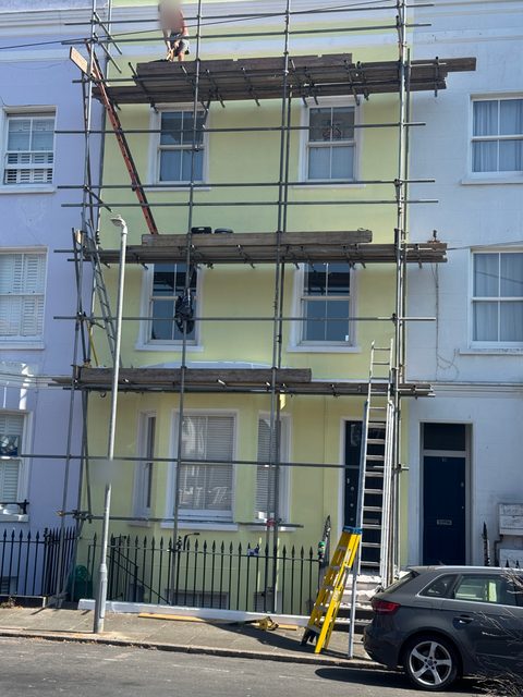 Storm Dry Roofing scaffold up the full height of a tall terraced house, with a worker on the top lift by the roof