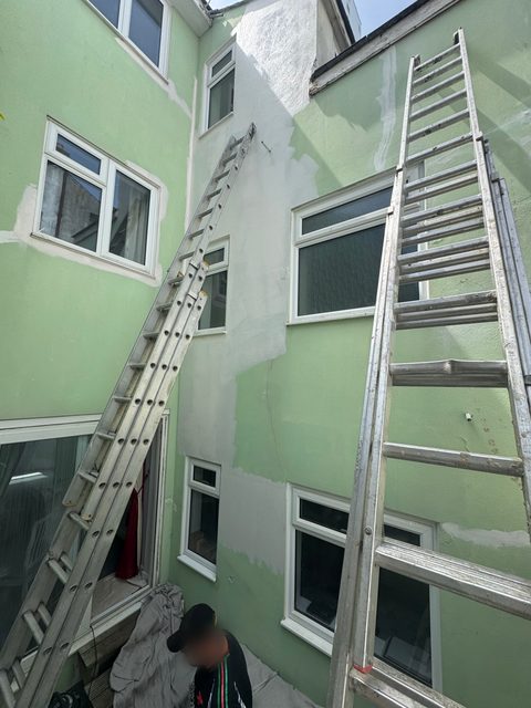 Storm Dry Roofing ladders set up the back wall of a tall rendered building to reach the roofline