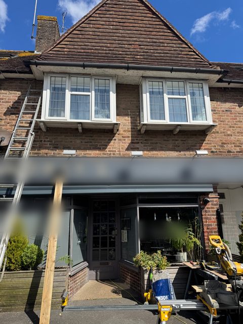 Storm Dry Roofing roofline job above a shopfront: ladders up to the fascia and soffit under the bay windows