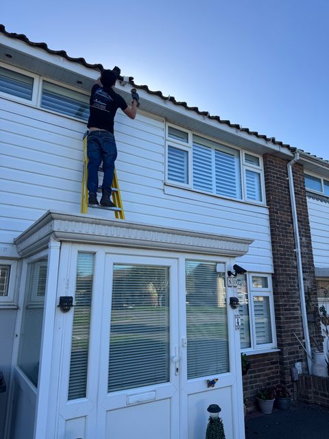 Storm Dry Roofing team member on a ladder working along the fascia and soffit of a white weatherboarded house
